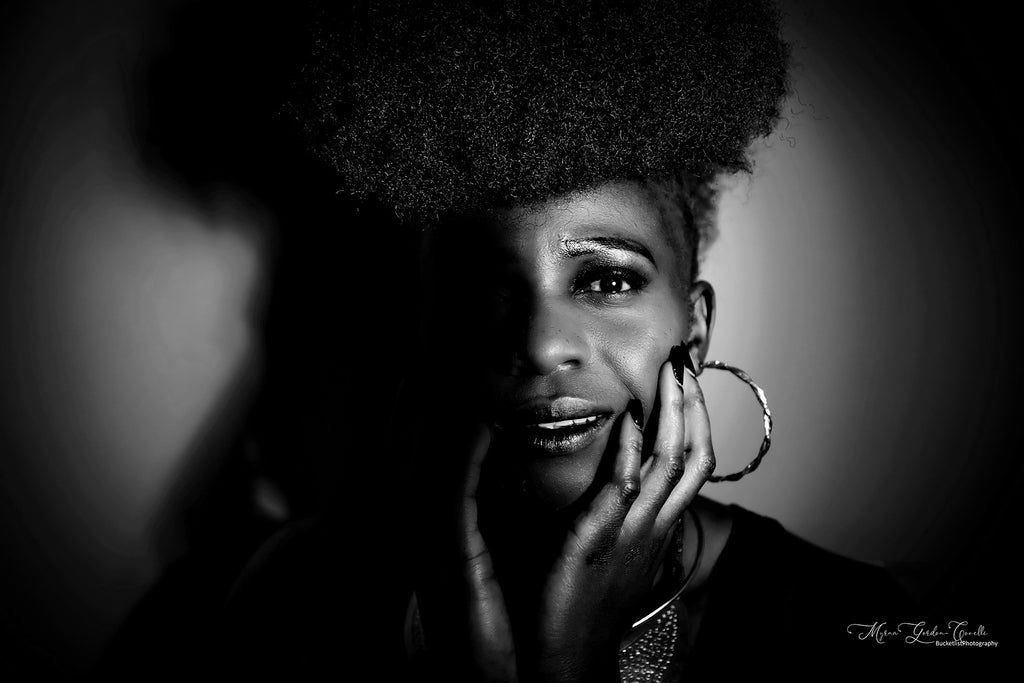 Black and white fine art portrait of Connie with natural afro, hand resting on cheek, hoop earring, dramatic chiaroscuro lighting celebrating African womanhood