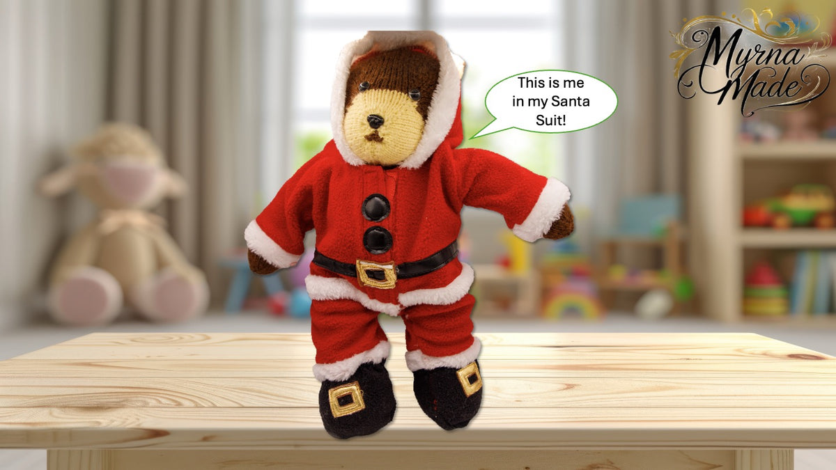Teddy bear in a Santa onezee with a speech bubble on a wooden table, blurred toys in the background.