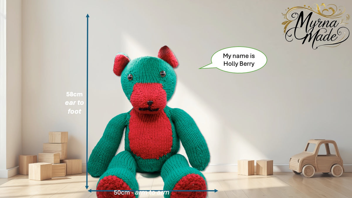 Knitted teddy bear with a speech bubble saying 'My name is Holly Berry' in a room with toys and a ruler for scale.