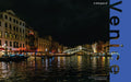 Rialto Bridge illuminated at night over the Grand Canal, Venice, with gondolas and lantern-lit waterfront